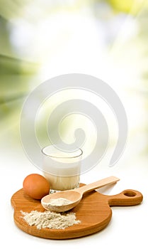 Milk, egg, flour, spoon and board on sun background