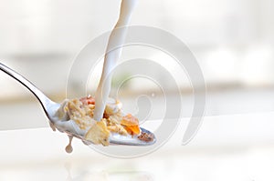 Milk falling on a spoon full of cereals in kitchen