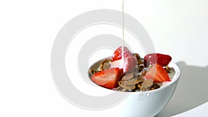 Milk falling in a wheat cereals and strawberries bowl