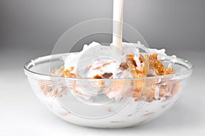 Milk flowing to the bowl with brown corn flakes