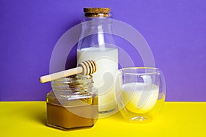 Milk in a glass and a bottle and a jar of honey on a fashionable yellow-purple background.