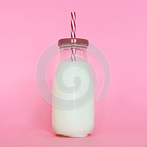 Milk glass bottle with straw isolated on pink background