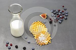 Milk in glass bottle. Waffles and berries on table