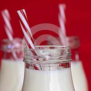 Milk in Glass Bottles with Red and White Straws over Red Background