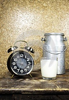 Milk in glass cup and aluminium can with alarm clock showing 7 o`clock on wood table, morning concept