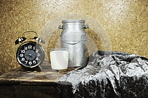 Milk in glass cup and aluminium can with alarm clock showing 7 o`clock on wood table, morning concept