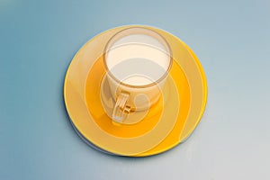 Milk in a glass cup on a yellow saucer