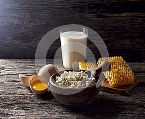 Milk in glass, honeycomb and eggs on a wooden background. Cottage cheese in a wooden bowl, rustic style. Dairy products in the mo