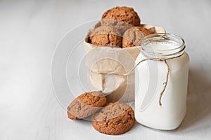 Milk in a glass jar and oatmeal cookies in a paper bag on a white table background. Copy, empty space for text