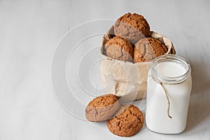 Milk in a glass jar and oatmeal cookies in a paper bag on a white table background. Copy, empty space for text