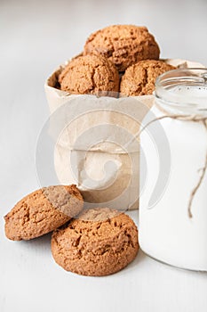 Milk in a glass jar and oatmeal cookies in a paper bag on a white table background. Copy, empty space for text