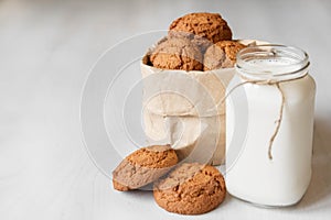 Milk in a glass jar and oatmeal cookies in a paper bag on a white table background. Copy, empty space for text