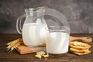 Milk in glass and jug with cookie on wooden table on grey background