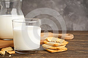 Milk in glass and jug with cookie on wooden table on a grey background, close-up