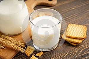 Milk in glass and jug with cookie on wooden table on a grey background, close-up