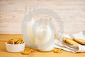 Milk in glass and jug with cookie on wooden table and light background, close-up