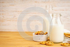 Milk in glass and jug with cookie on wooden table and light background, space for text.