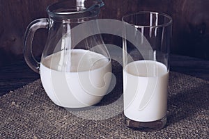 Milk in a glass and jug on a wooden table.