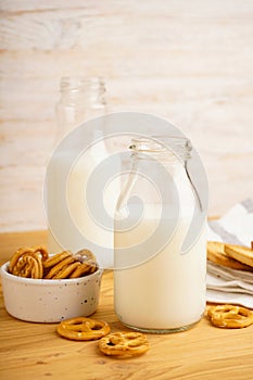 Milk in jug with cookie on wooden table and light background, vertically, close-up