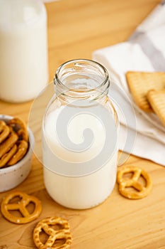 Milk in jug with cookie on wooden table and light background, vertically, close-up