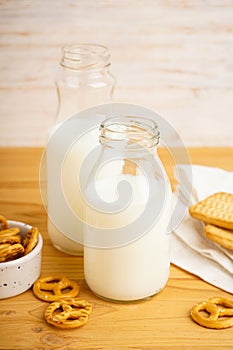 Milk in jug with cookie on wooden table and light background, vertically, close-up