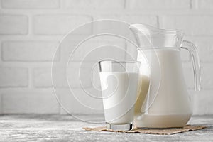 milk in jug and glass on table with white brick wall as background