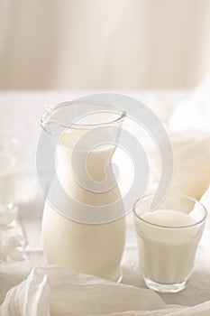 Milk in a jug and glasses on a white background. Tablecloth. Flowers . copy space