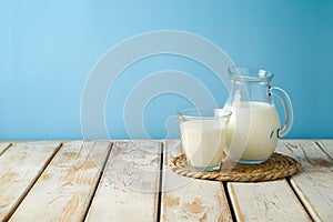 Milk jug and milk glass on wooden table over blue background. Kitchen mock up for design