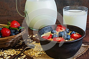Milk in a jug and oatmeal porridge with glass of milk in a pottery bowl with fresh ripe berrie