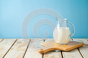 Milk jug on wooden table with tablecloth and cutting board over blue background. Kitchen mock up for design