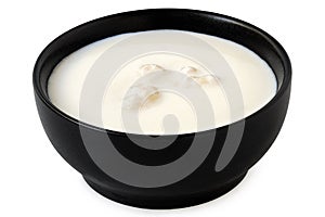 Milk with kefir grains in a black ceramic bowl isolated on white