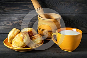 Milk mug and yellow plate with homemade donuts on dark vintage boards. Idea for a delicious festive breakfast or dinner