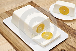 Milk orange jelly square shape on a white platter on a wooden table