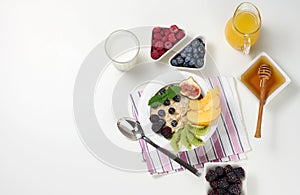 Milk, plate with oatmeal porridge and fruit, freshly squeezed juice in a transparent glass decanter, honey in a bowl on a white