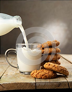 Milk is poured from a bottle into a glass and next to it is a stack of cookies on a wooden table