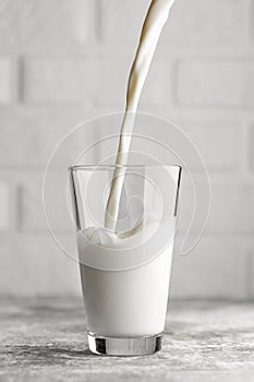 milk pouring in big glass on table with white brick wall as background