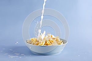 Milk pouring into the blue bowl of cornflakes, milk splashes around the plate on the blue background