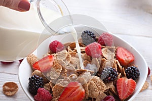Milk pouring into bowl of cereals with fresh berries