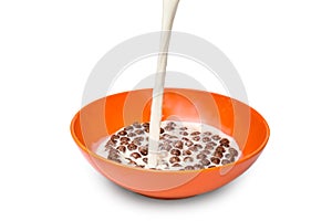 Milk pouring into the bowl with chocolate cereal balls on white background