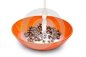 Milk pouring into the bowl with chocolate cereal balls on white background