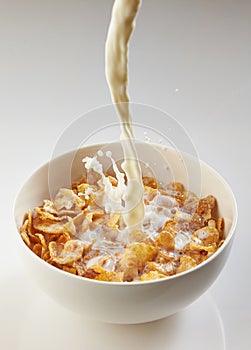 Milk pouring into bowl with corn flakes