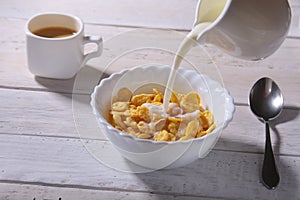 Milk pouring into a bowl of delicious corn flake cereals and cap with espresso coffee. Morning breakfast.