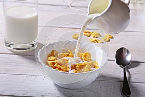 Milk pouring into a bowl of delicious corn flake cereals and cap with espresso coffee. Morning breakfast.