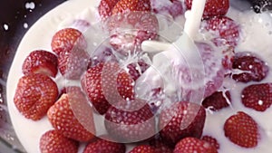 Milk pouring into bowl with fresh stawberries