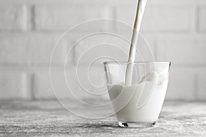 milk pouring in glass on table with white brick wall as background