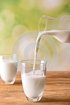 Milk pouring from jug into glass on wooden table