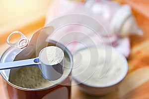 Milk powder in spoon with can and baby bottle milk in bowl on wooden table