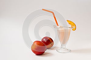 Milk refreshing cocktail with nectarine in a beautiful figured glass with an orange tube and a piece of fruit on the glass, two ma