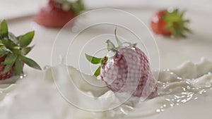 Milk splash on a ripe red strawberry fruit, which lies on a white plate with milk. Slow motion. A few berries lie on the