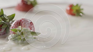 Milk splash on a ripe red strawberry fruit, which lies on a white plate with milk. Slow motion. A few berries lie on the
